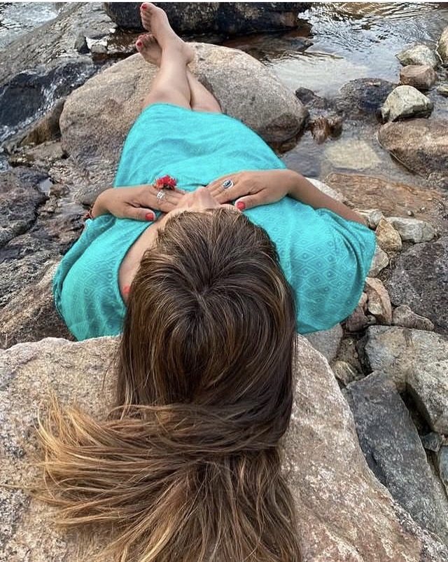 Claudia recostada sobre una roca junto al agua, con las manos sobre el vientre