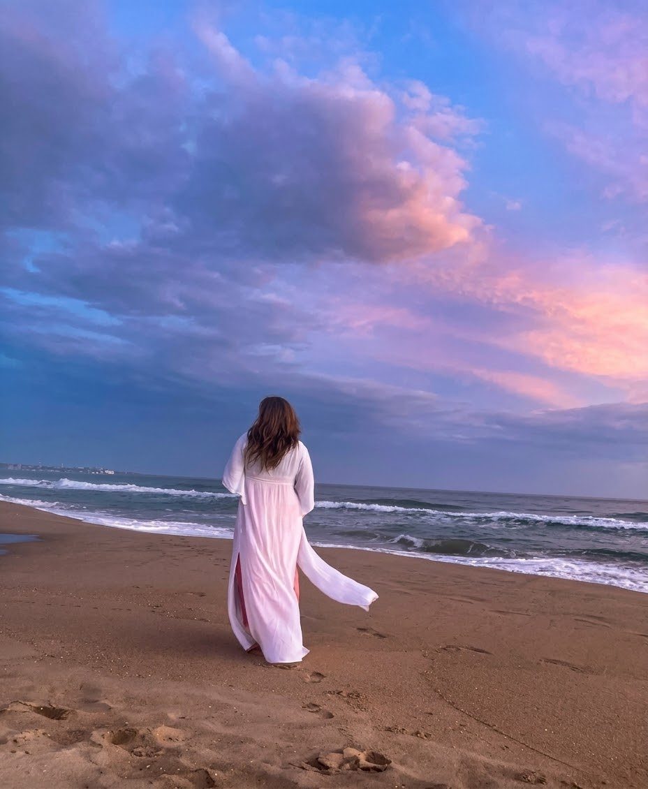 Claudia caminando por la orilla del mar al atardecer, con un vestido blanco